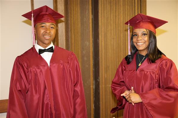 Two Alabama School for the Deaf graduates smile at the camera while wearing their maroon caps and gown.